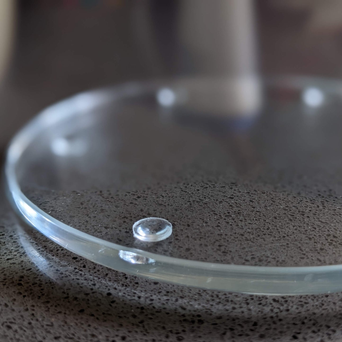 A clear glass coaster with bumper feet adhered to the base to prevent slipping and sliding.