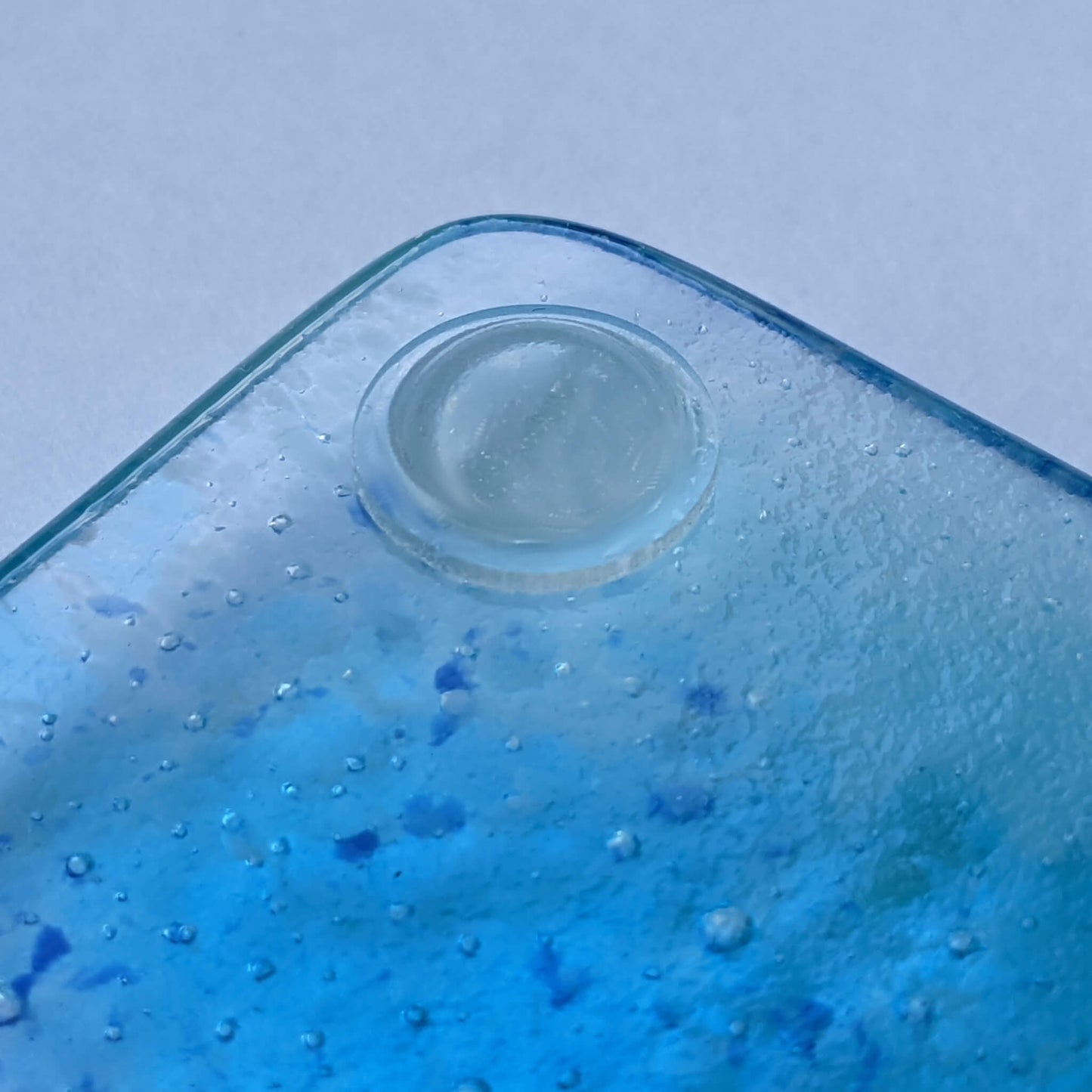 A single clear domed bumper foot being used on a fused glass coaster.