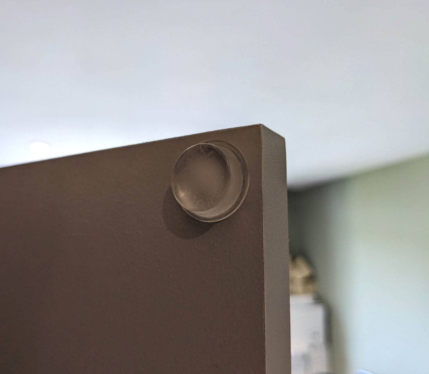 A clear flat topped bumper foot utilised on a cabinet door to prevent banging noise when the door is being closed.