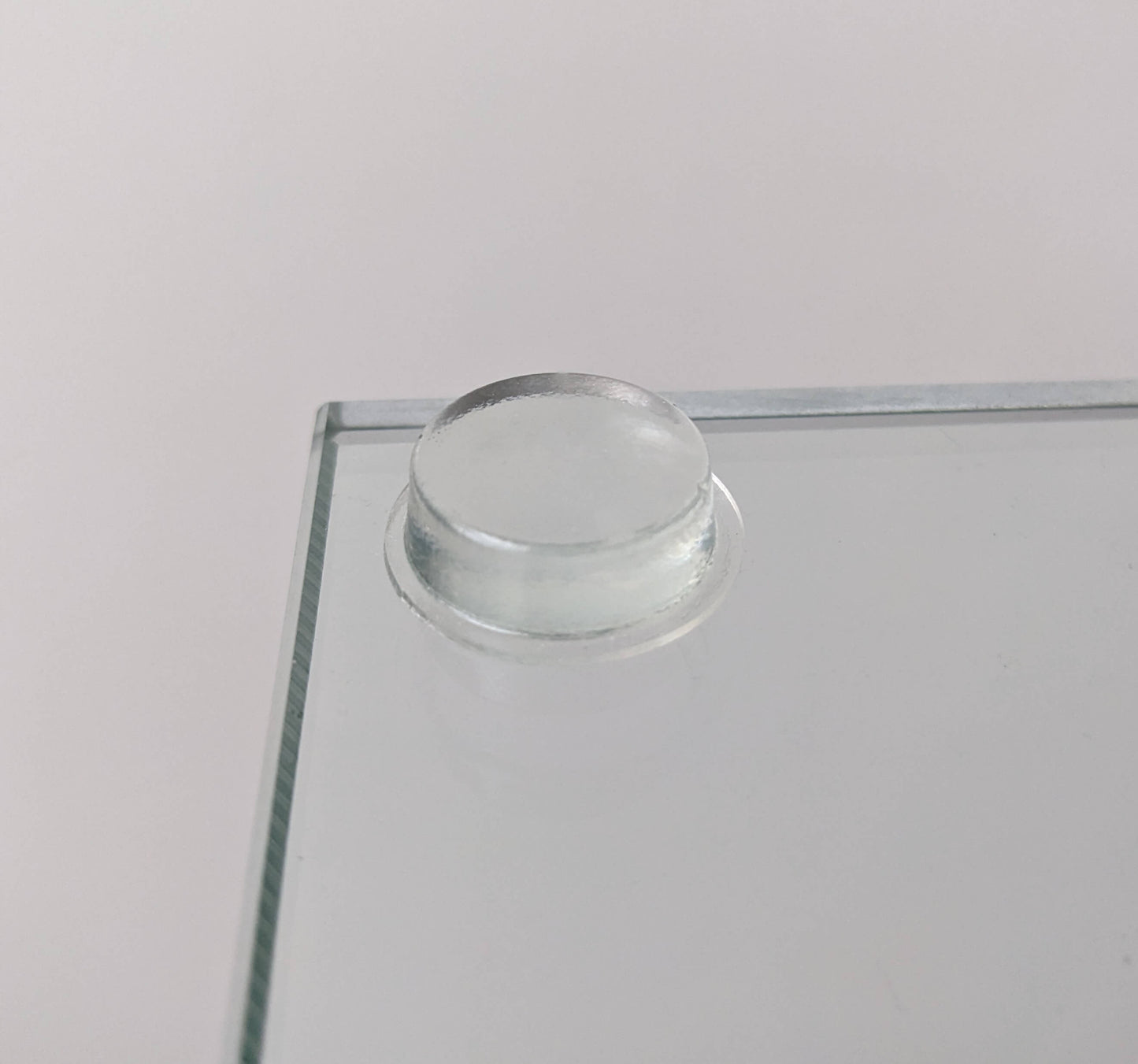 A clear flat topped bumper adhered to a piece of glass.