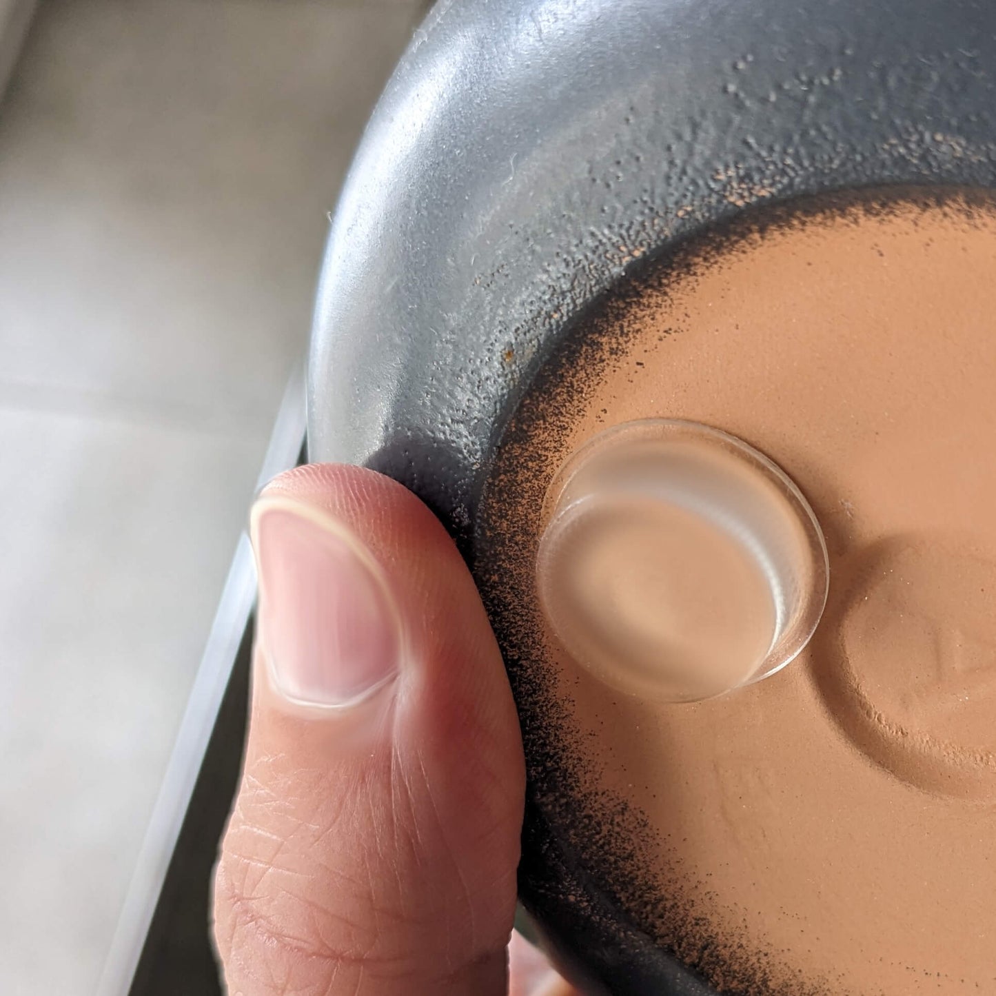 A mans finger applying a clear flat bumper pad to the base of a ceramic pot.