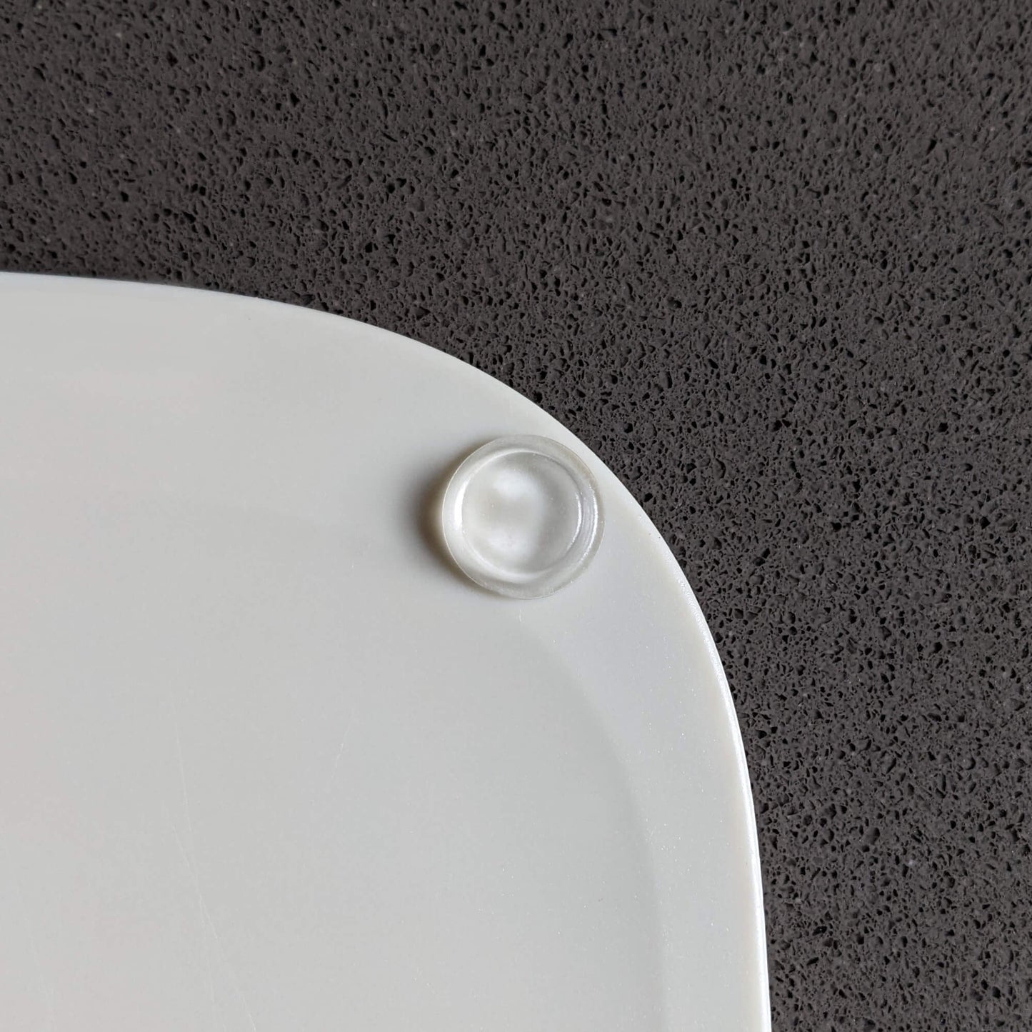 A clear flat bumper pad stuck on a plastic chopping board to prevent the board sliding.