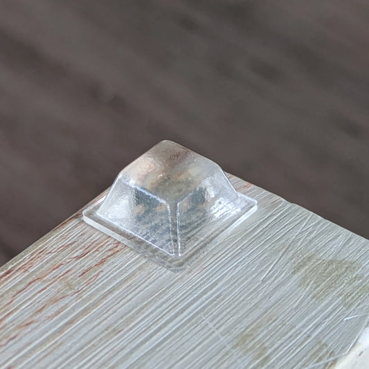 A single clear flat topped square bumper affixed to the corner of a wooden chopping board.