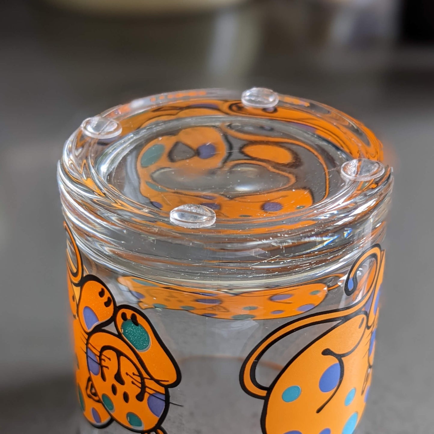 Four clear domed bumper feet used on the underside of a glass cup that has cartoon cats as decorations.