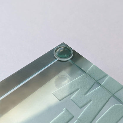 A clear domed bumper foot used on the corner of a glass paperweight.