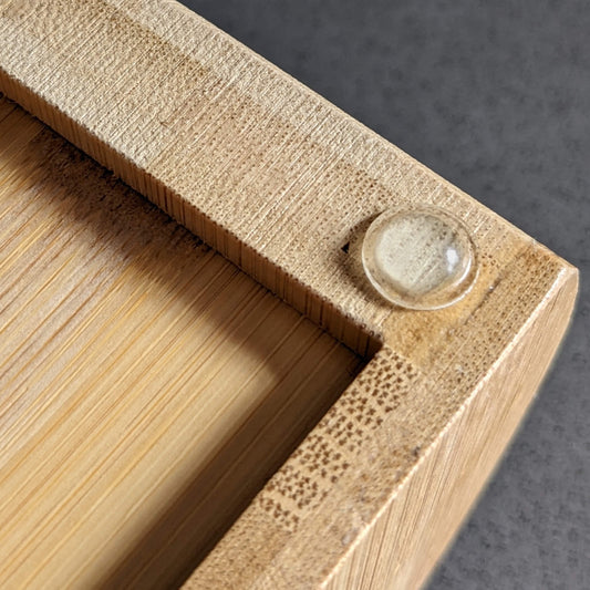 A domed bumper foot used on the bottom corner of a wooden desk organiser.