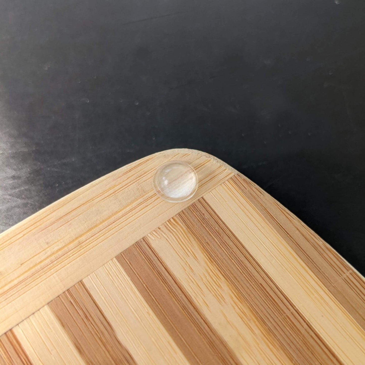 Domed bumper foot used on the corner of a wooden chopping board to prevent sliding.