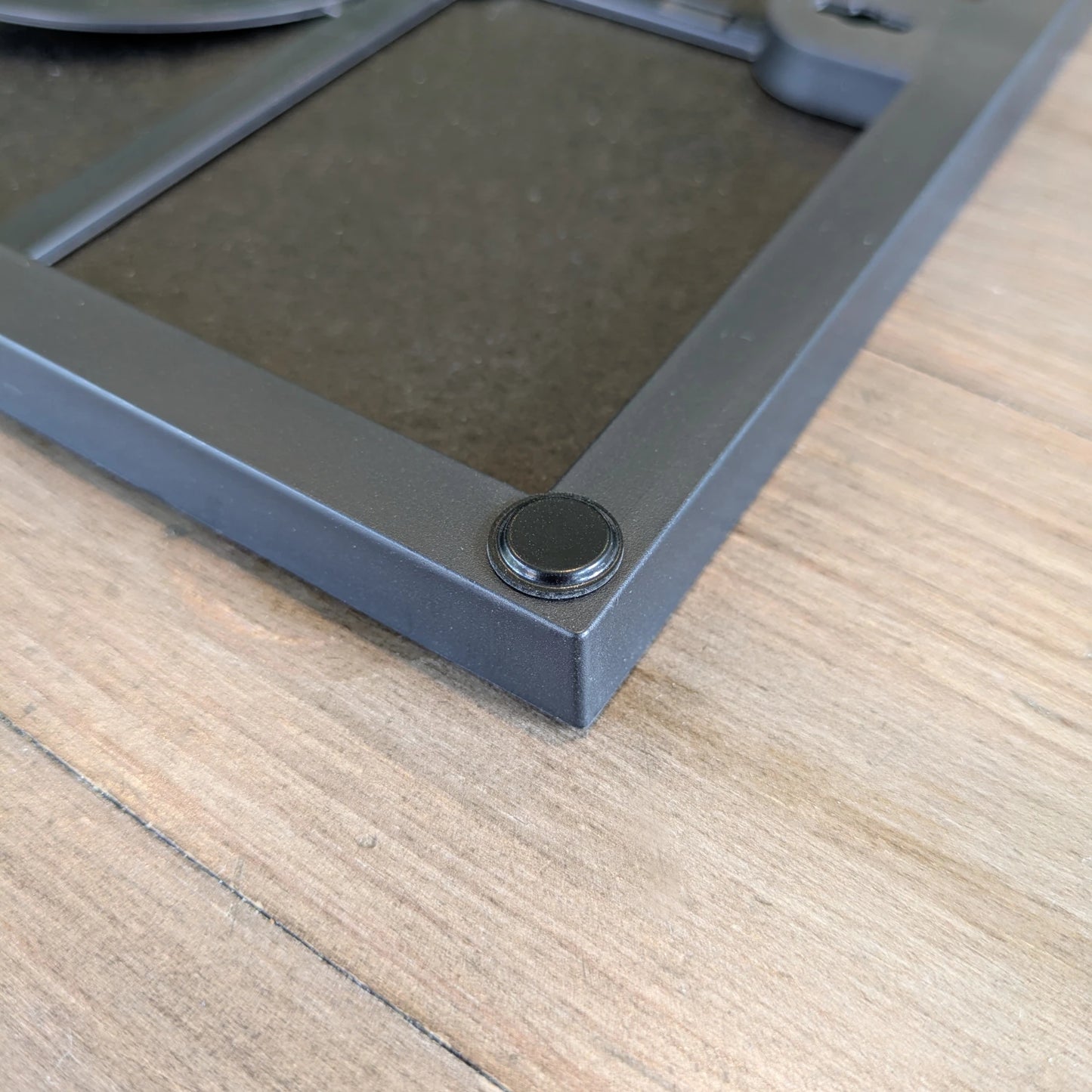Flat topped black finish bumper pad used on the edge of a picture frame to prevent wall marking or damage.