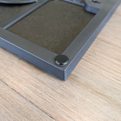 Flat topped black finish bumper pad used on the edge of a picture frame to prevent wall marking or damage.