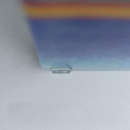 A clear flat bumper pad used on a glass coaster to help prevent movement.
