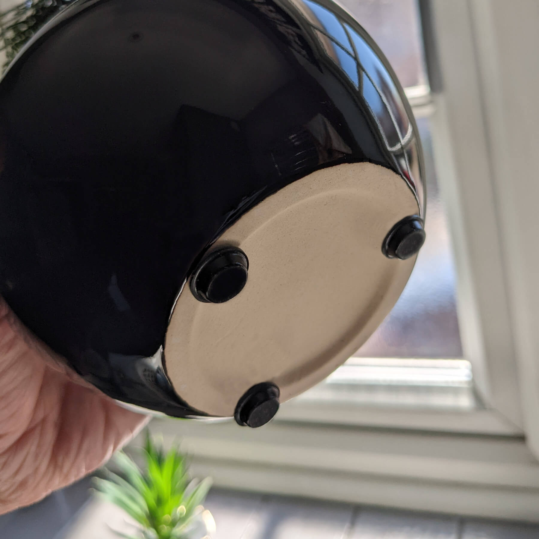 A ceramic plant pot with 3 black flat topped bumper feet adhered to the base to help stop damage to surfaces.