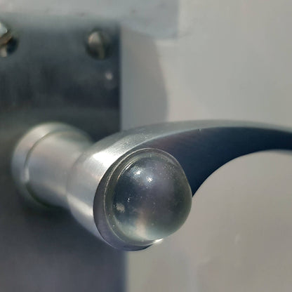 A domed bumper foot applied to a metal door handle, to stop the handle damaging a nearby wall when it makes contact.