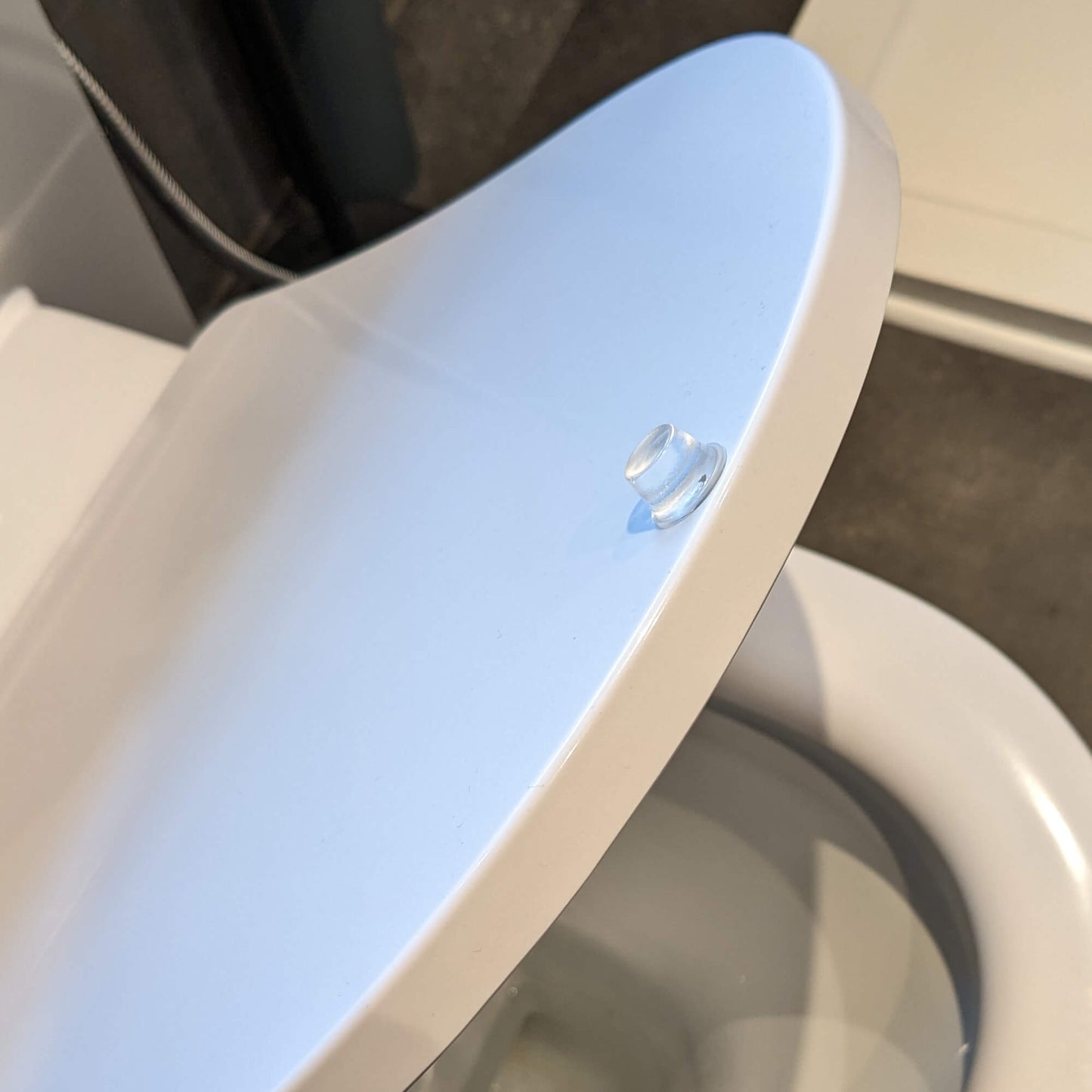 A tall bumper foot used on the top of a toilet seat lid to stop banging noise when the lid makes contact with a bathroom unit.