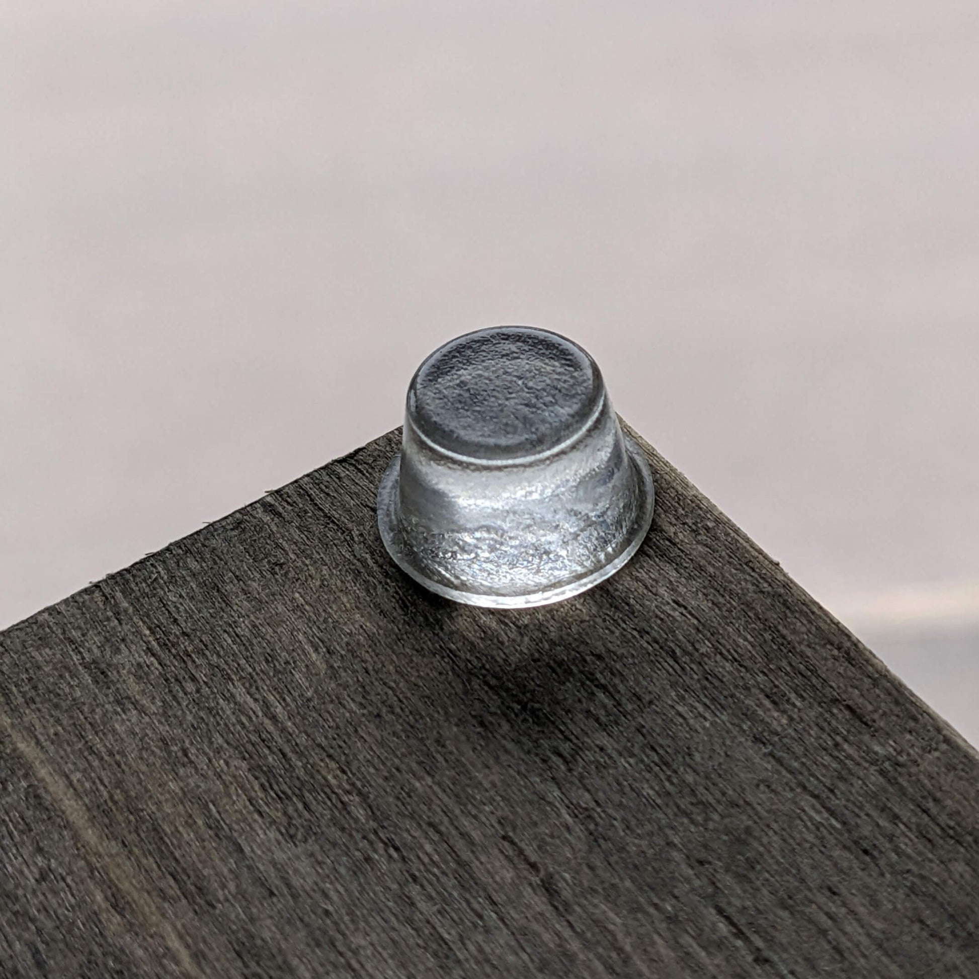 A clear tall bumper foot used on the corner of a wooden unit to give it stability.